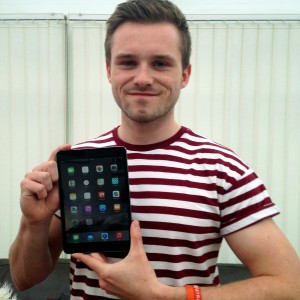 Photo of a person with short hair holding up an iPad and smiling into the camera