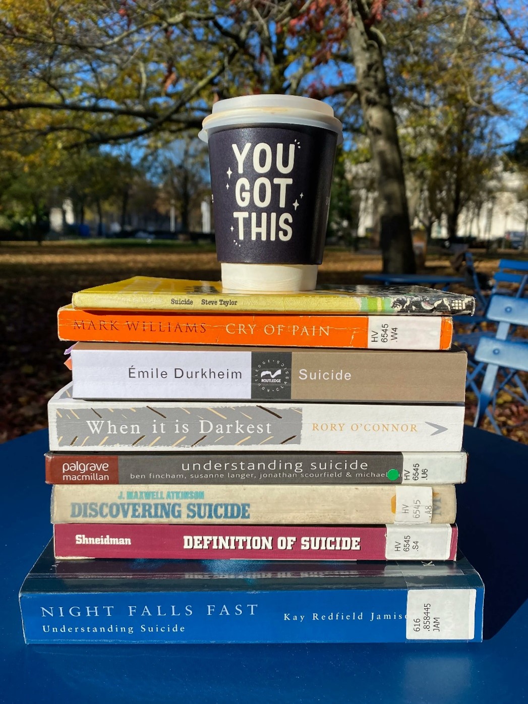 Coffee cup reading 'You got this' atop a pile of books.