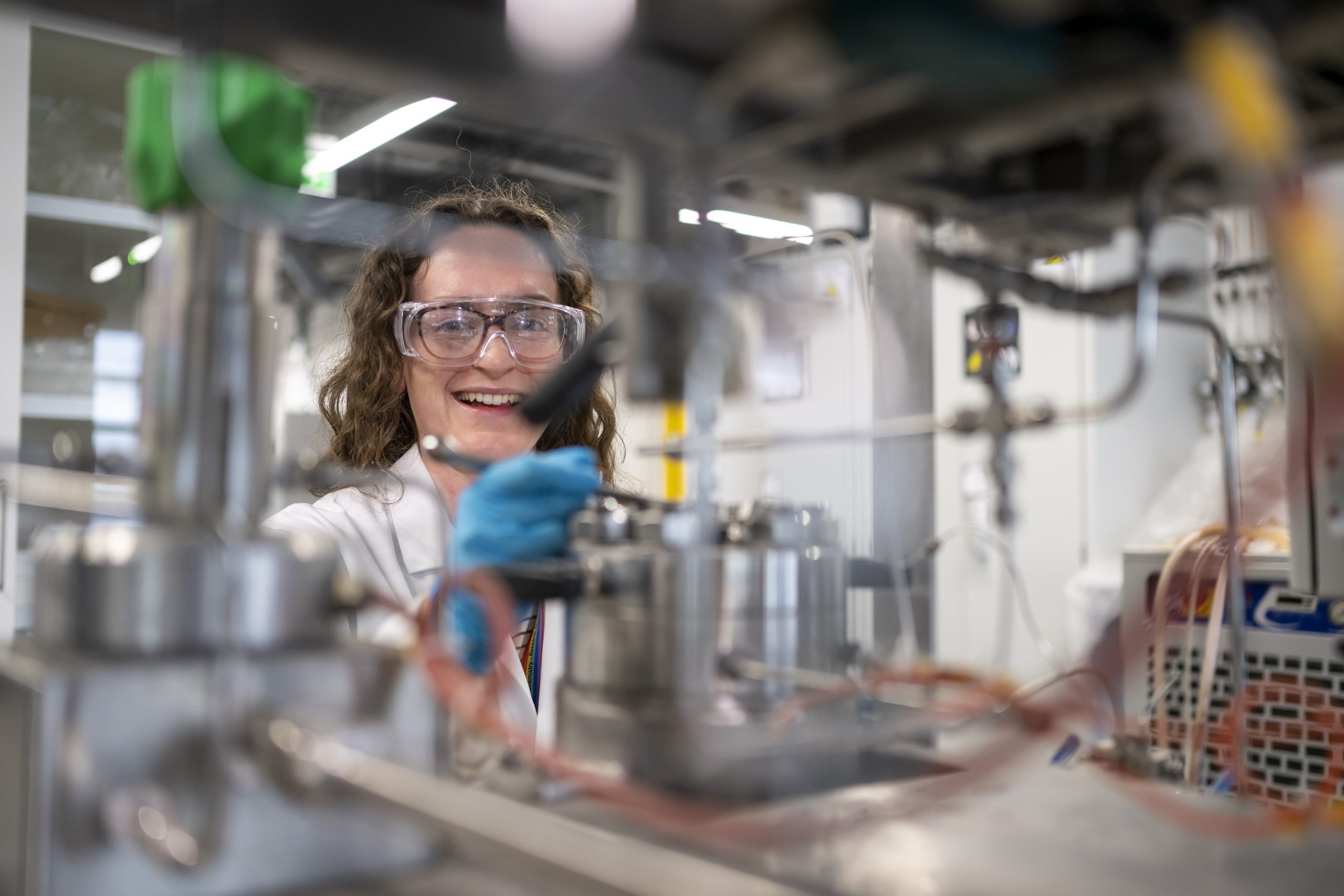 Young woman is wearing a white lab coat and googles inside the Translational Research Hub lab at Cardiff University
