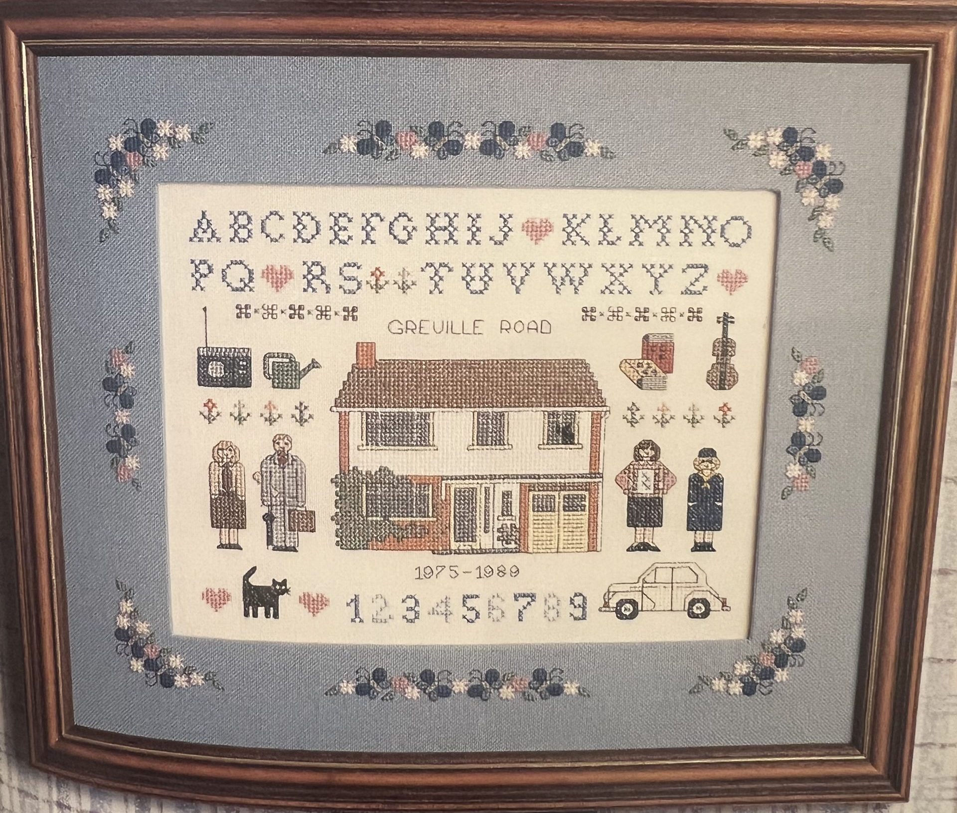 Embroidery sampler of a family with their house in the centre, family members either side, pets and hobbies around