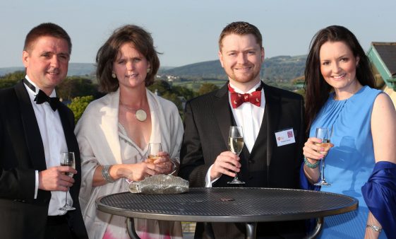Four smiling people gathered around a table holding up glasses of champagne.
