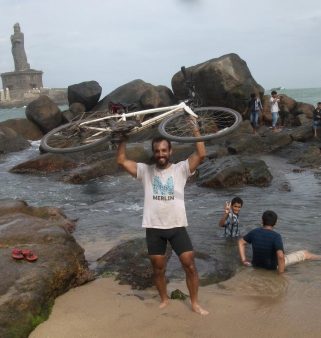 A man standing at the shore holding a bike over his head.