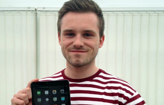 Portrait shot of a person with short hair holding an iPad and smiling into the camera