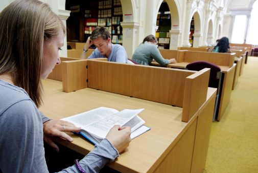 Female student reading a book in a library.