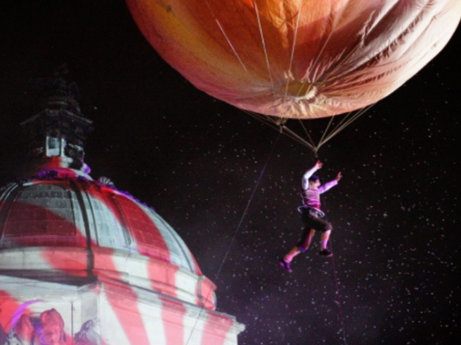 City of the Unexpected - an image of a performer attached to a giant peach near Cardiff's City Hall