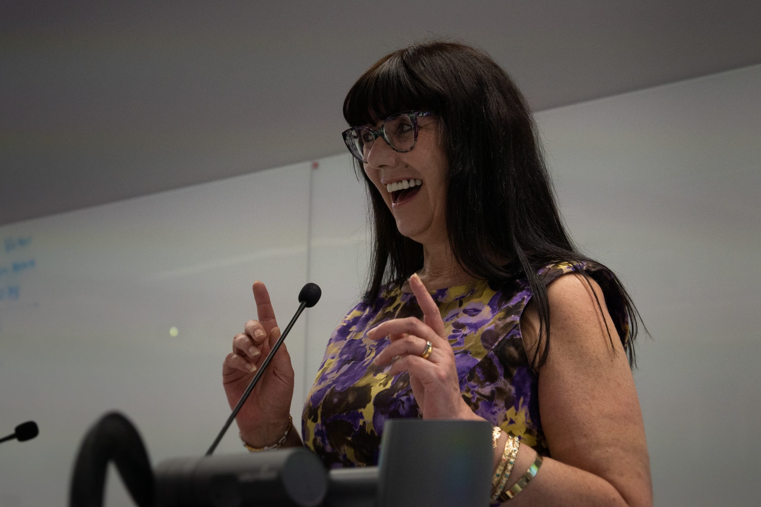 A lady with dark hair abd glasses stabds at a lectern to perform her poem