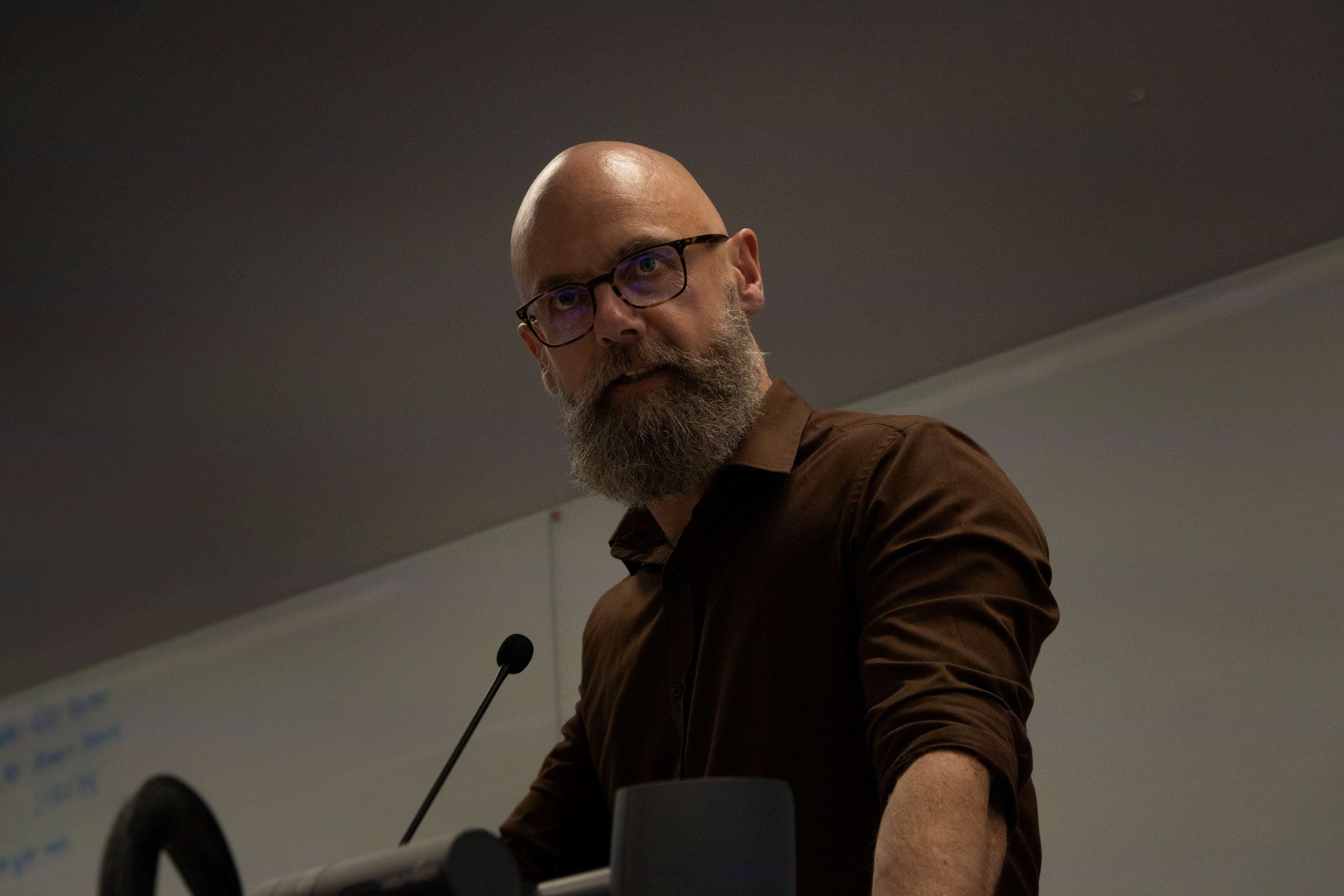 A man with a beard and glasses stands at a lectern