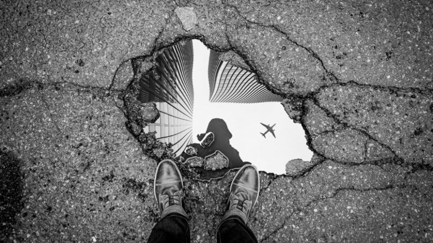 Puddle on the ground reflecting a plane in the sky