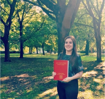 Charlotte standing in the park holding her dissertation.