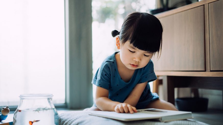 Little girl looking down and reading a book, representing the company handbook