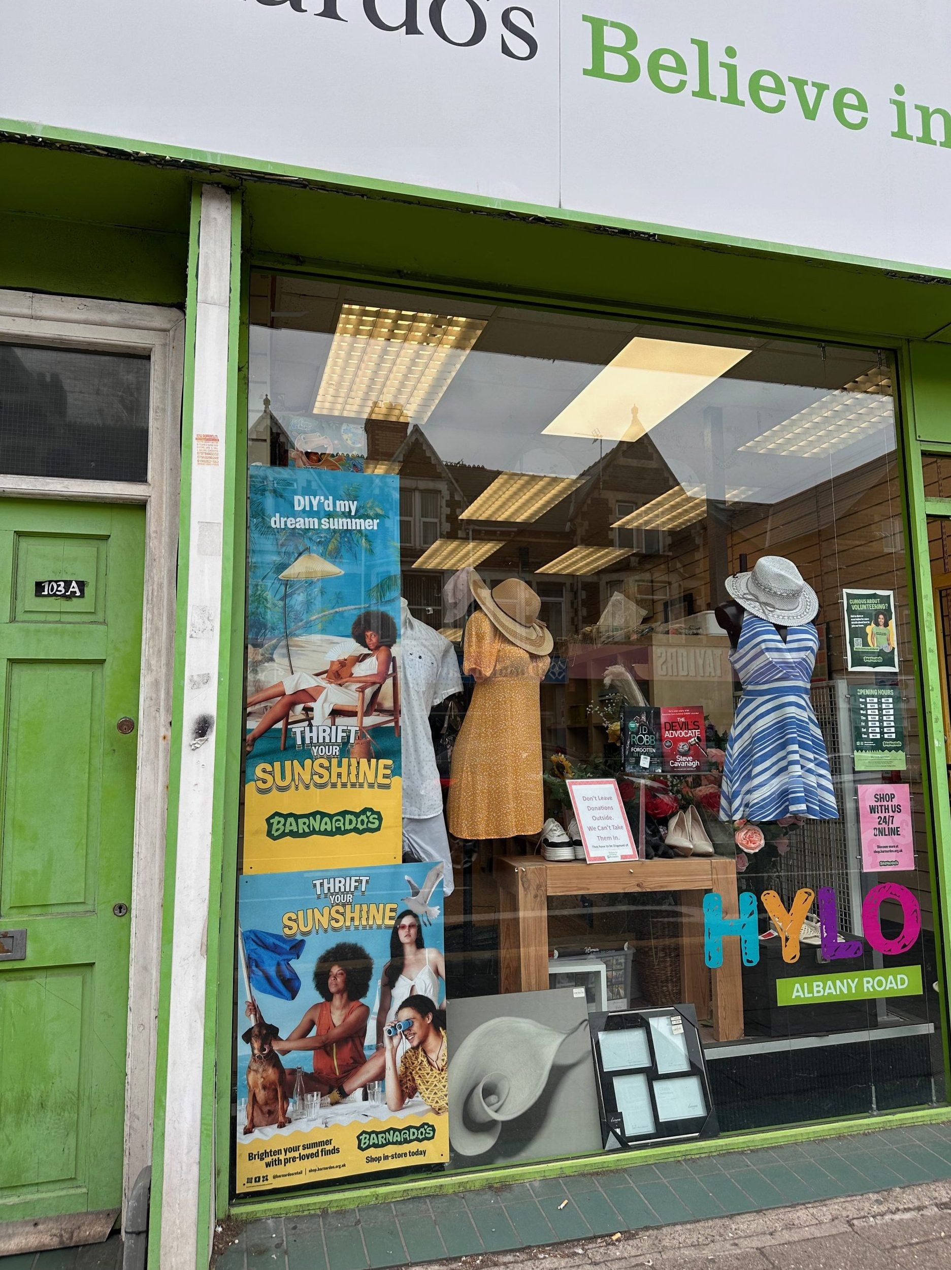 Photograph of Barnado's charity shop front window with display of summer posters, sundresses and sunhats