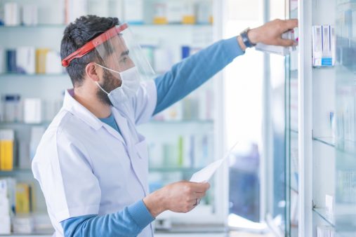 Pharmacist wears protective mask at work gives prescription medicine