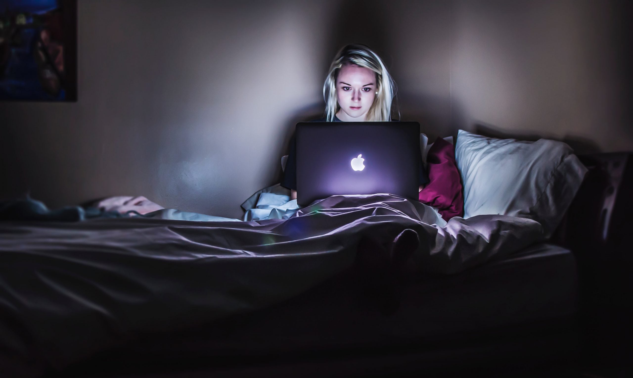 a blonde woman works in bed at a laptop