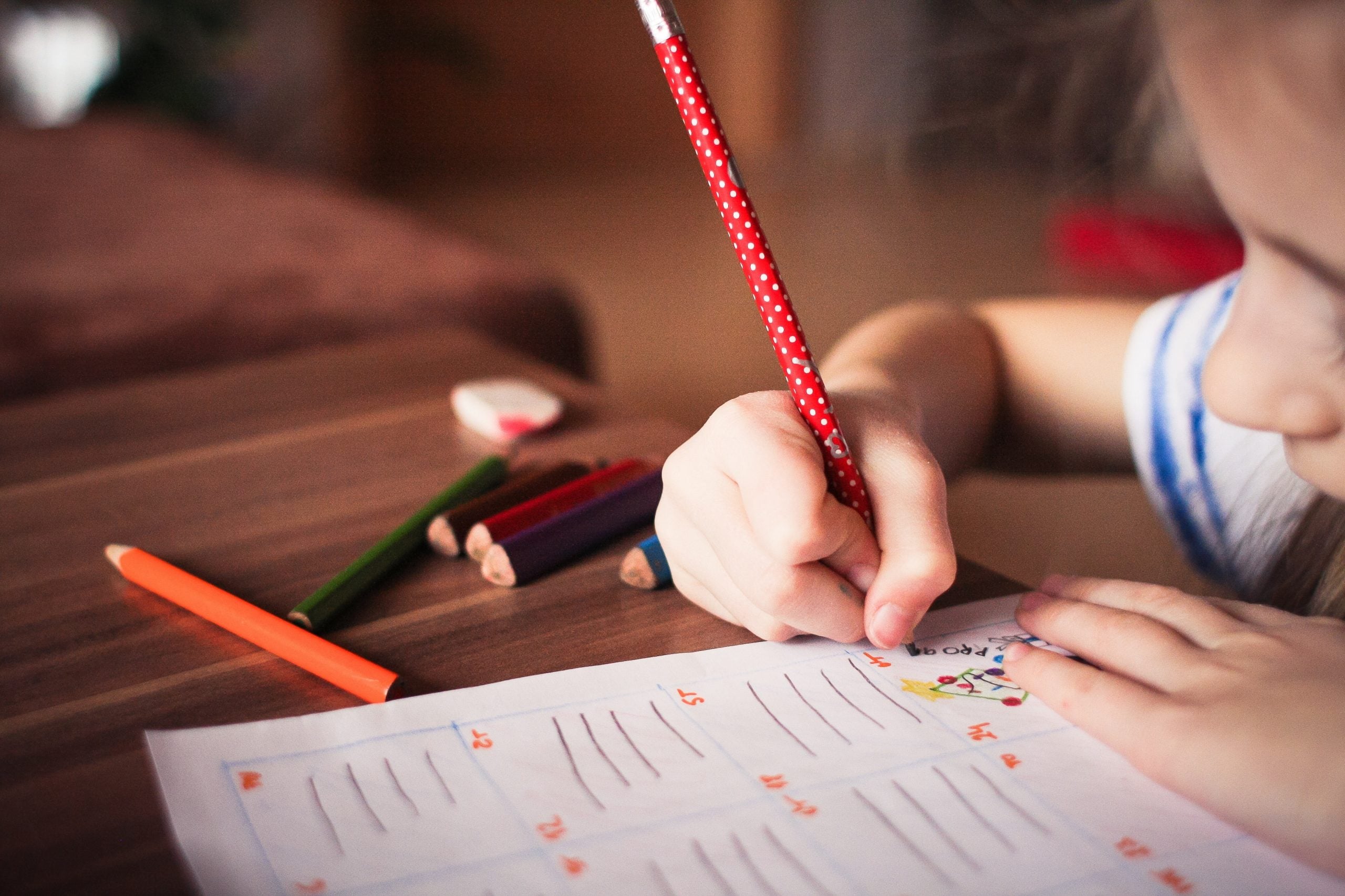 a child holding a red pencil writing on a piece of paper